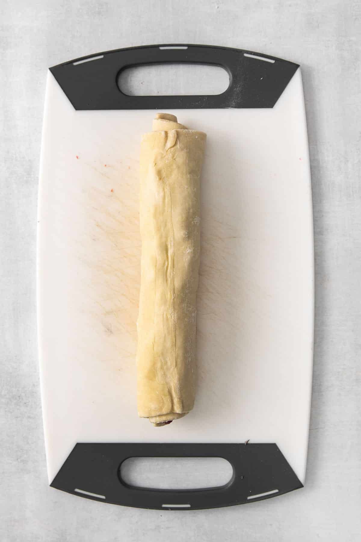 puff pastry dough rolled up on a white cutting board.