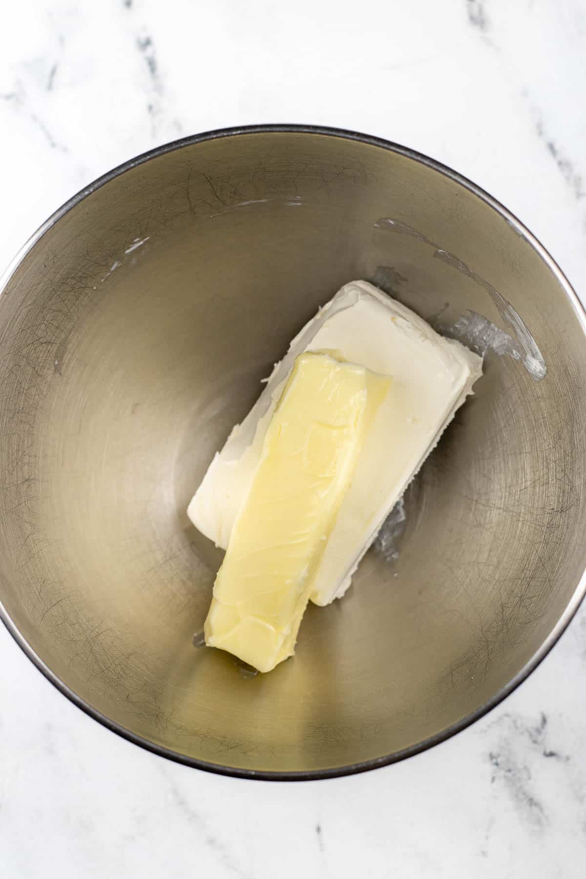 silver mixing bowl with cream cheese block and a stick of butter.