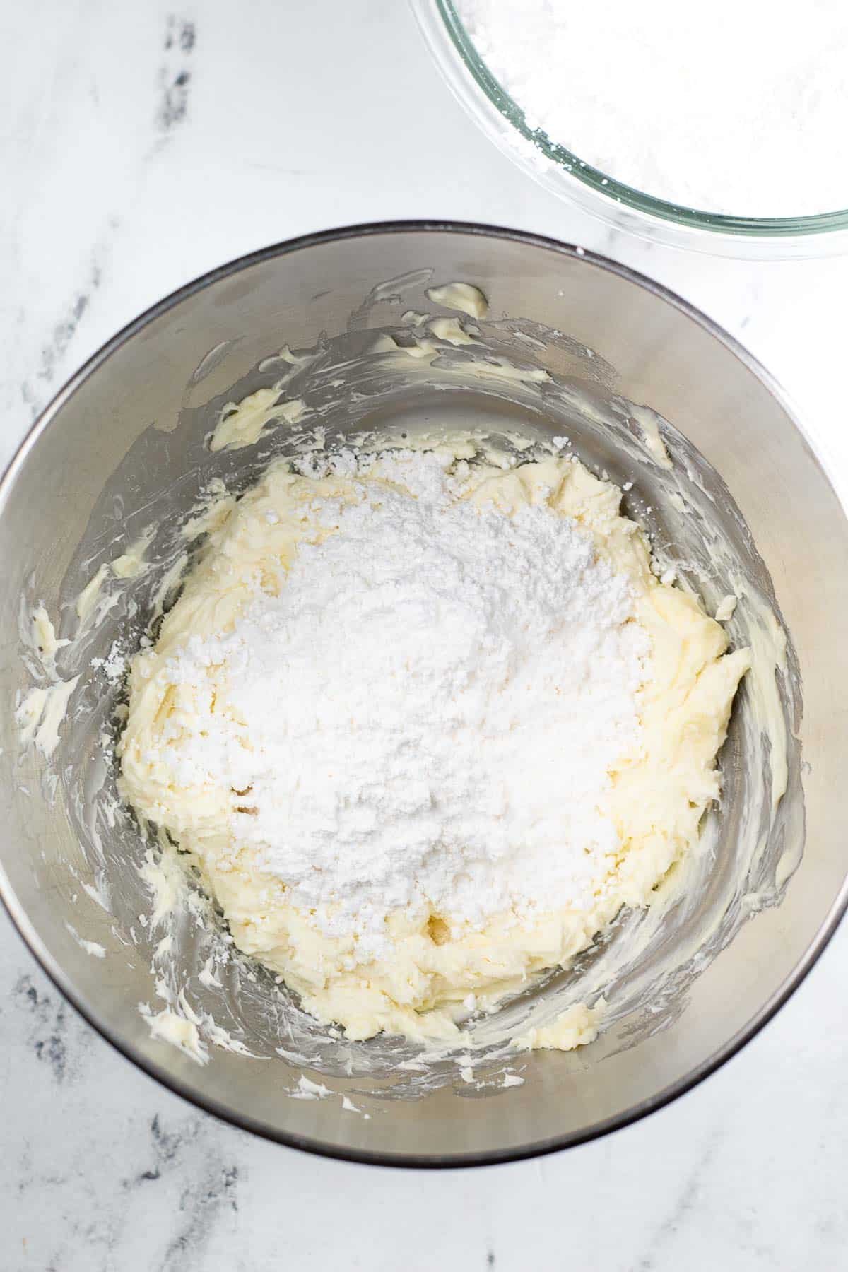 silver mixing bowl with powdered sugar over cream butter mixture.