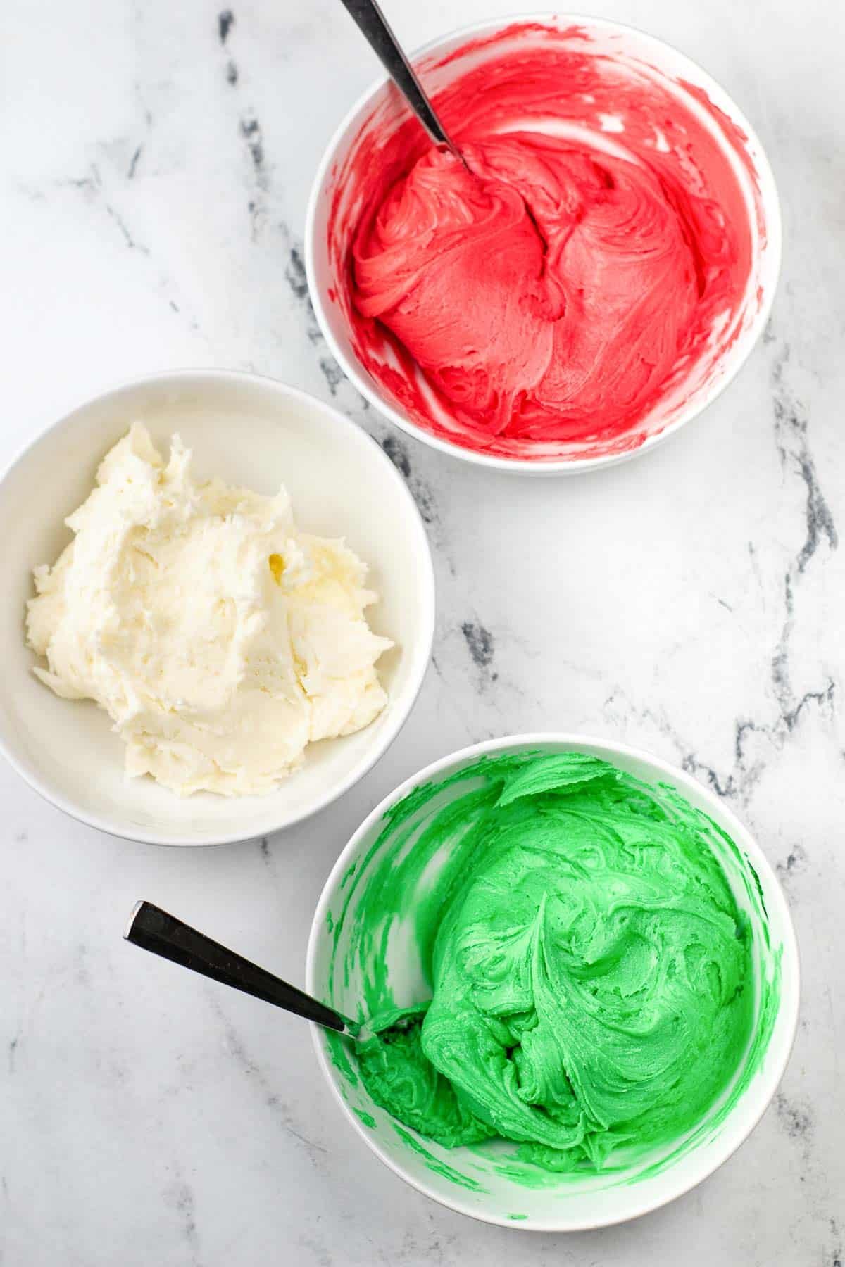 three small white bowls with dough for cream cheese mints. one green one red and one white.