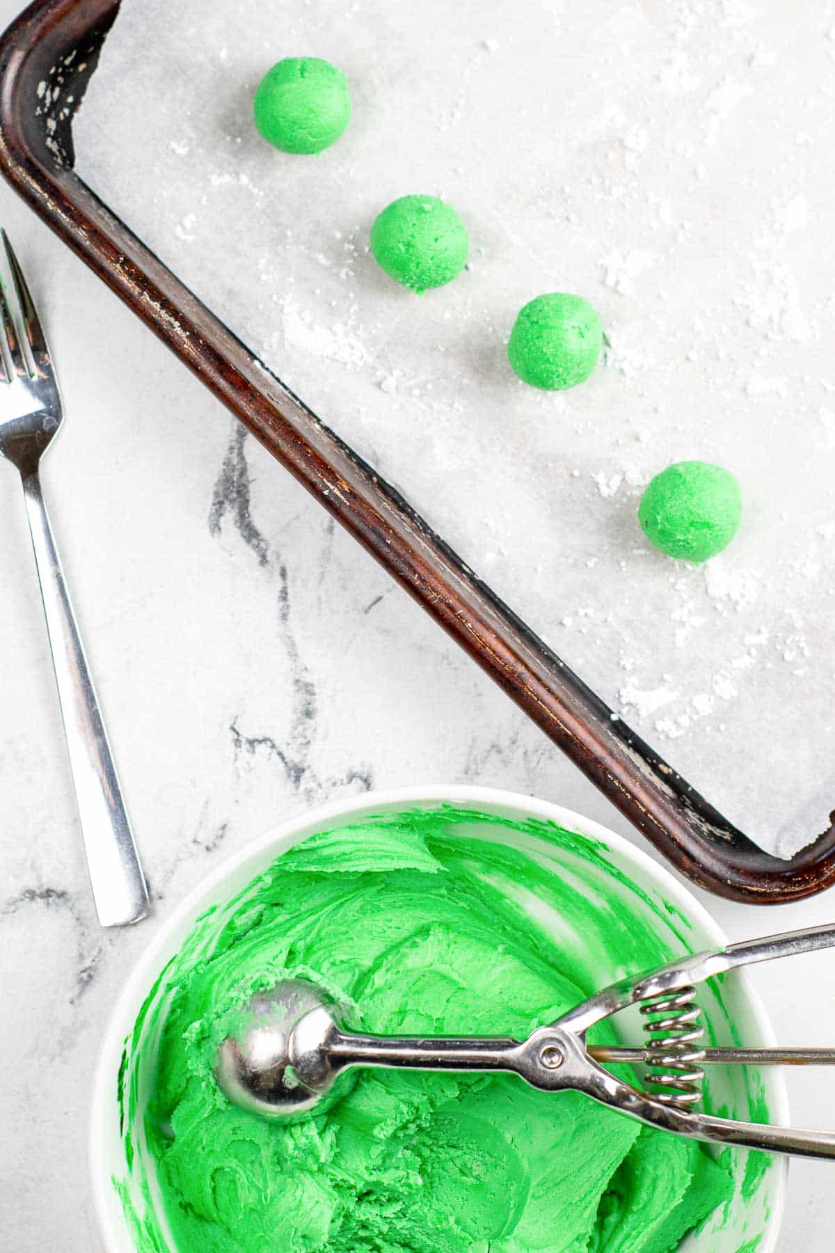 bowl of green butter mints batter with a cooking sheet with four balls of green batter.