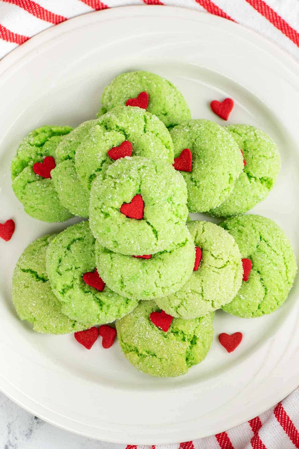 white plate full of green crinkle cookies with a red little heart in the center.