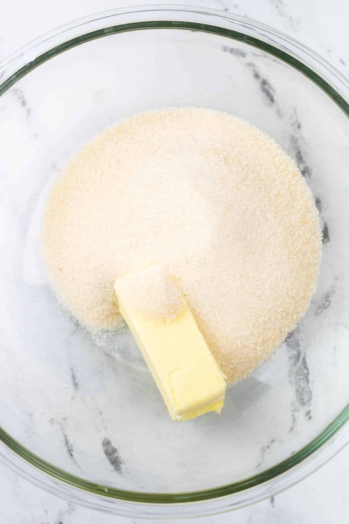 glass mixing bowl with sugar and a stick of butter.