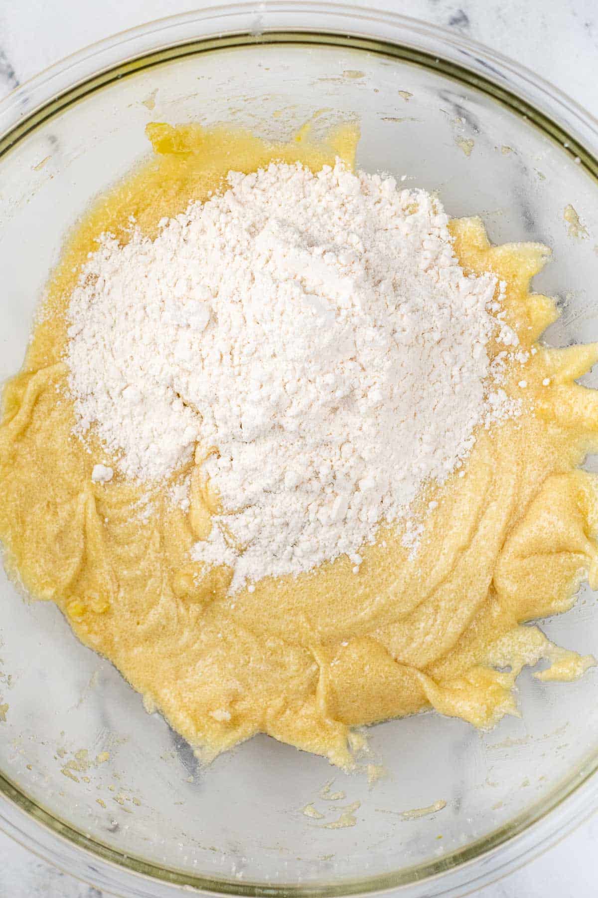 glass bowl of creamed egg, butter and sugar with flour on top.