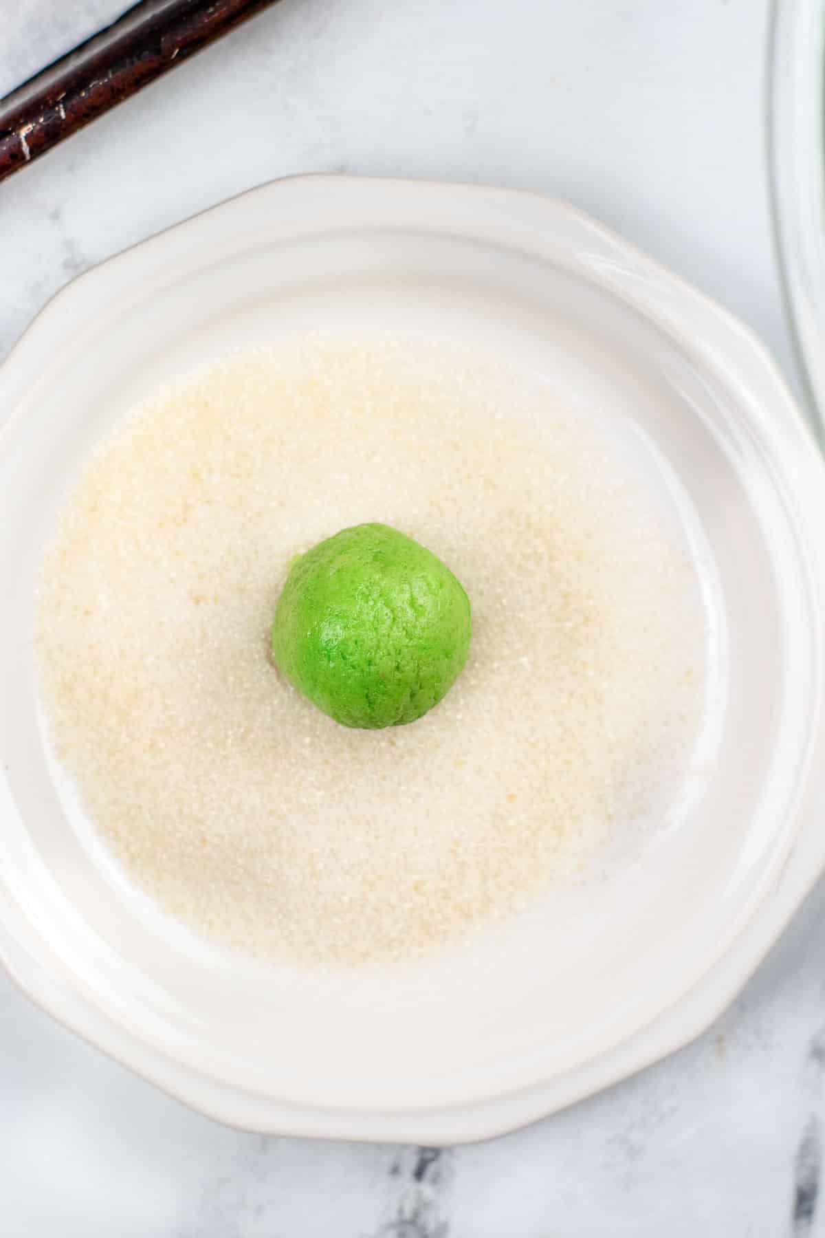white plate of sugar with a green cookie dough ball in the center.