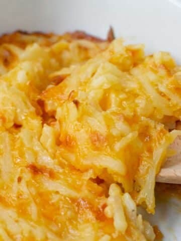 closeup of a scoop of hashbrown casserole on a wooden spoon.