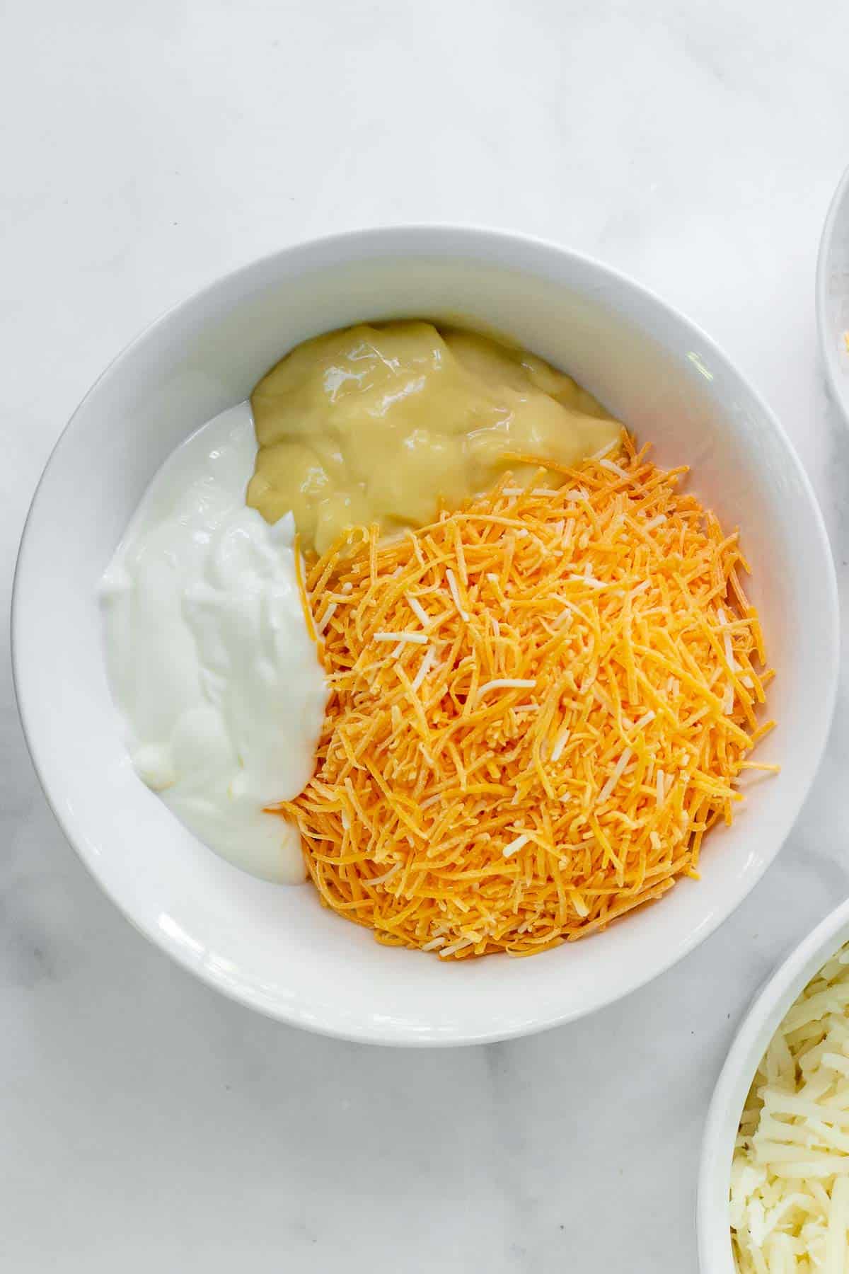 white bowl with shredded cheese, cream of chicken soup, and sour cream.