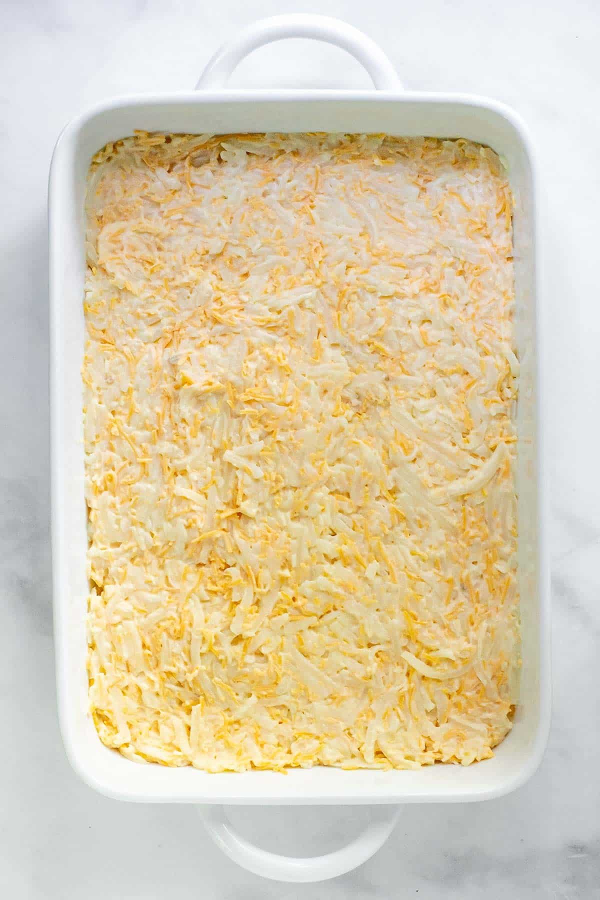 white rectangle casserole dish with hash brown and cheese mixture spread evenly.