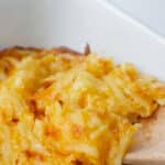 closeup of cheesy hashbrown casserole being scooped with a wooden spoon.