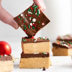 two squares of chocolate peanut butter bars with another bar being held over top of the stack.