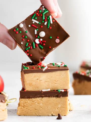 two squares of chocolate peanut butter bars with another bar being held over top of the stack.