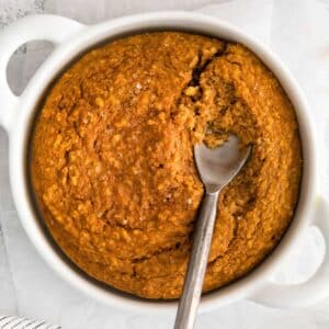 closeup of pumpkin oatmeal in a white bowl with a spoon in.