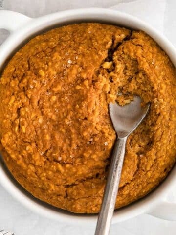 closeup of pumpkin oatmeal in a white bowl with a spoon in.