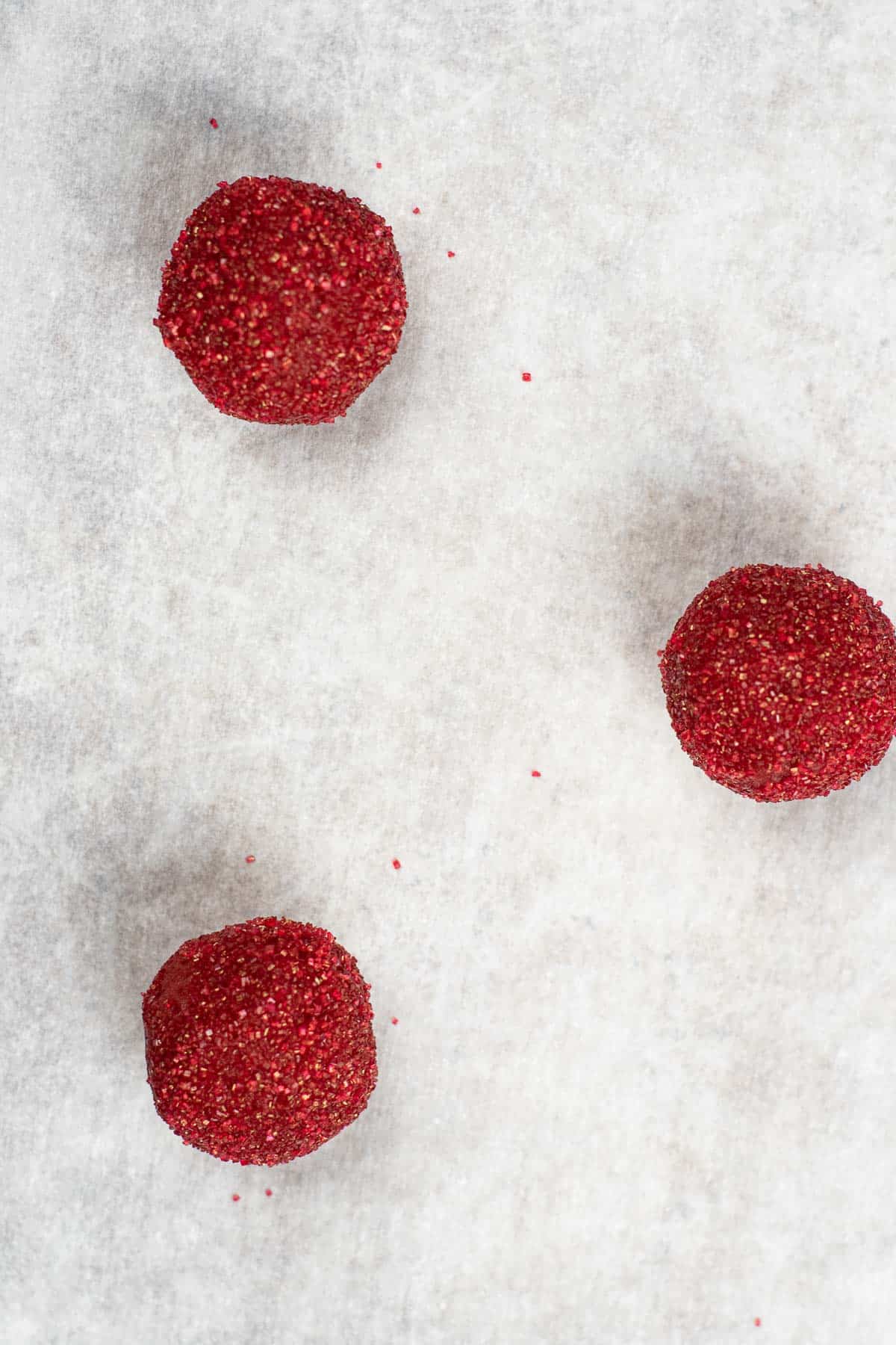 three red sugar coated cookie dough balls on white parchment paper.