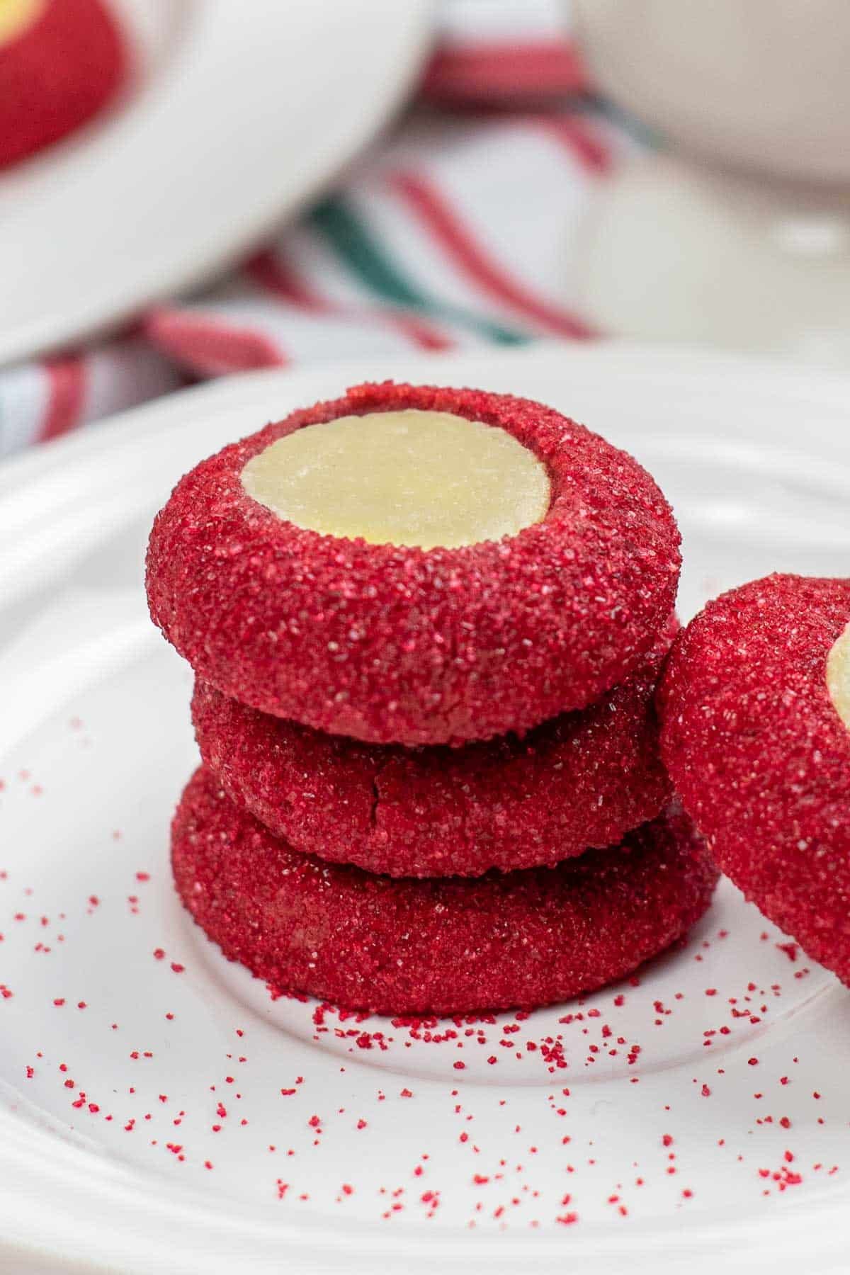stack of three red sugar coated red velvet cookies with cream cheese mixture in the center.