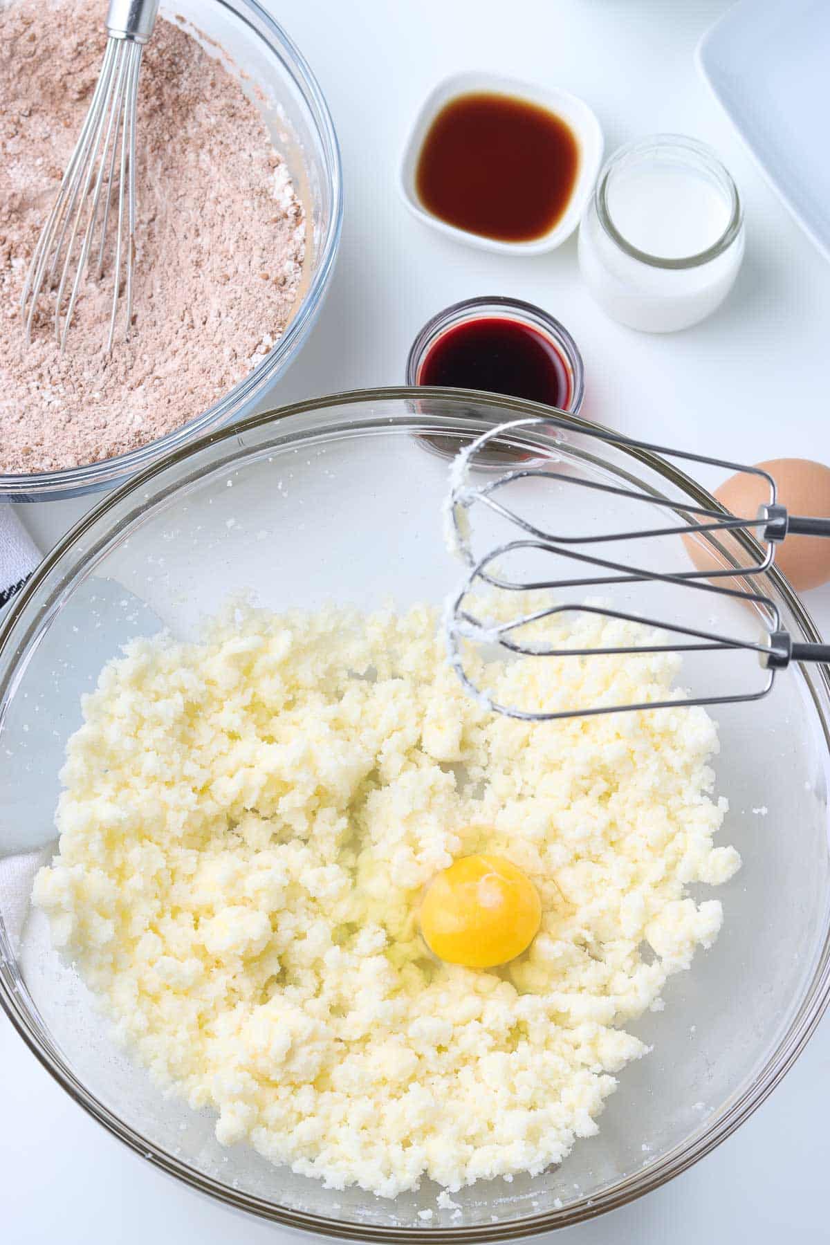 glass mixing bowl with creamed butter and sugar with a raw egg over top.
