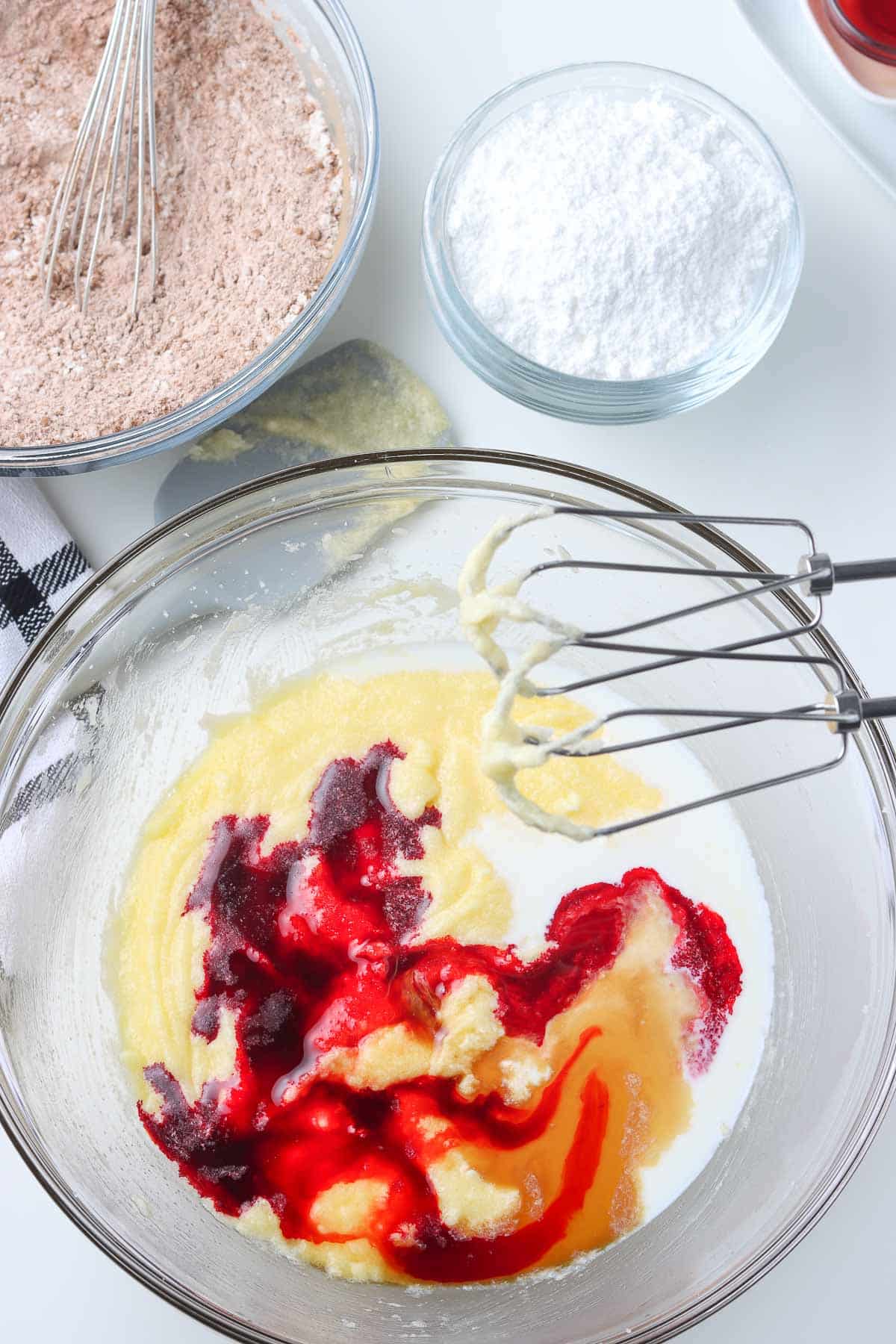 glass mixing bowl with red food coloring over creamed egg, butter and sugar.