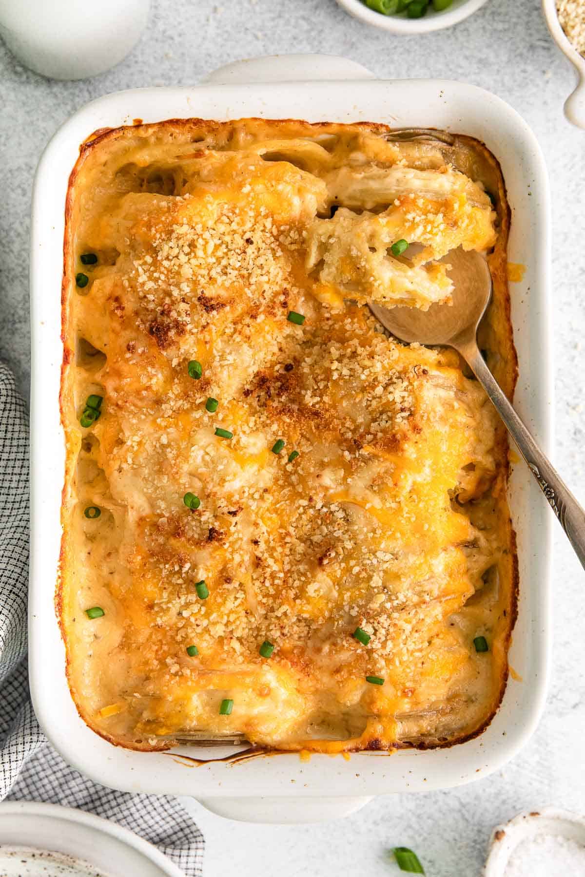 cheesy scalloped potatoes in a casserole dish with a spoon scooping.