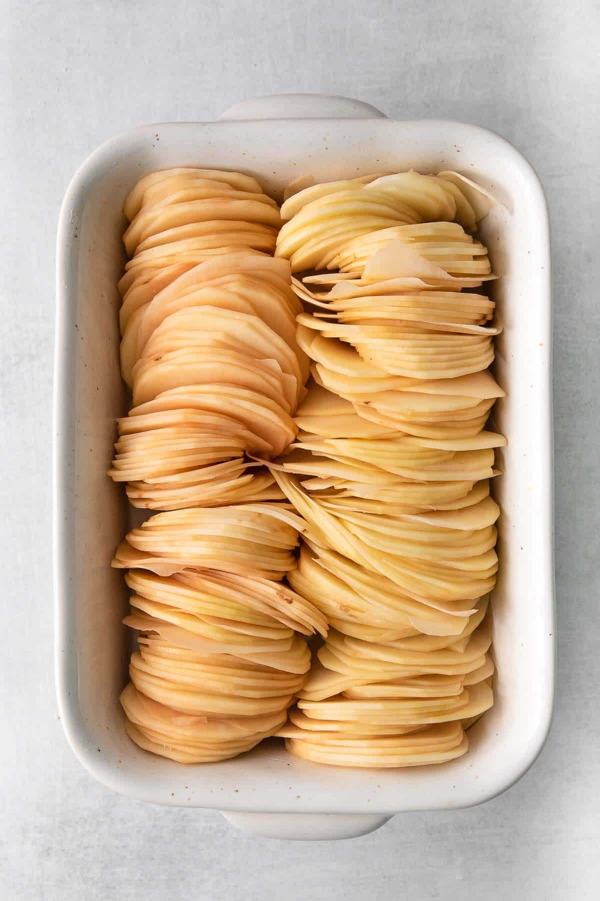 thinly sliced potatoes in a white rectangle baking sheet.