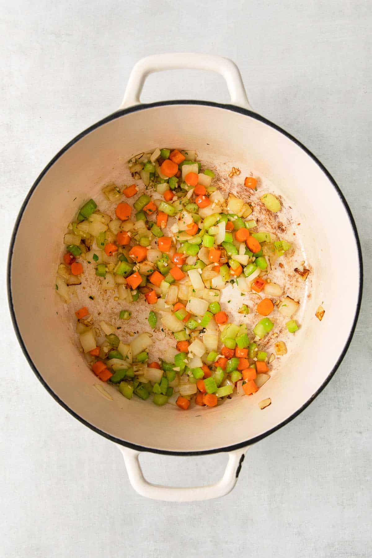 white dutch oven with diced carrots, celery and onions sauteing.