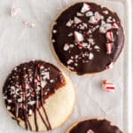 three chocolate dipped shortbread cookies topped with crushed peppermints on white parchment paper