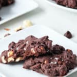 two chocolate peanut clusters on a white plate with one cut in half.