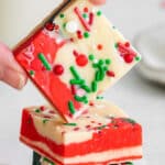 stack of red, white and green christmas fudge with a piece being held over top by a woman's fingers