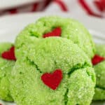 closeup of green crinkle cookie with a red candy heart in the center with text overlay that reads Grinch Crinkle Cookies