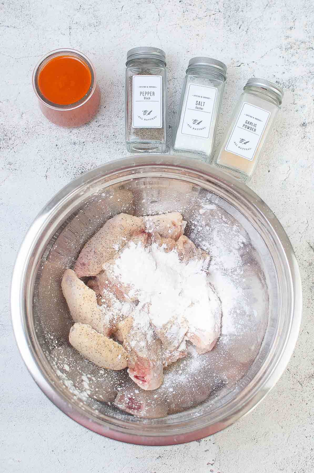 silver mixing bowl with uncooked chicken wings with cornstarch sprinkled over top.