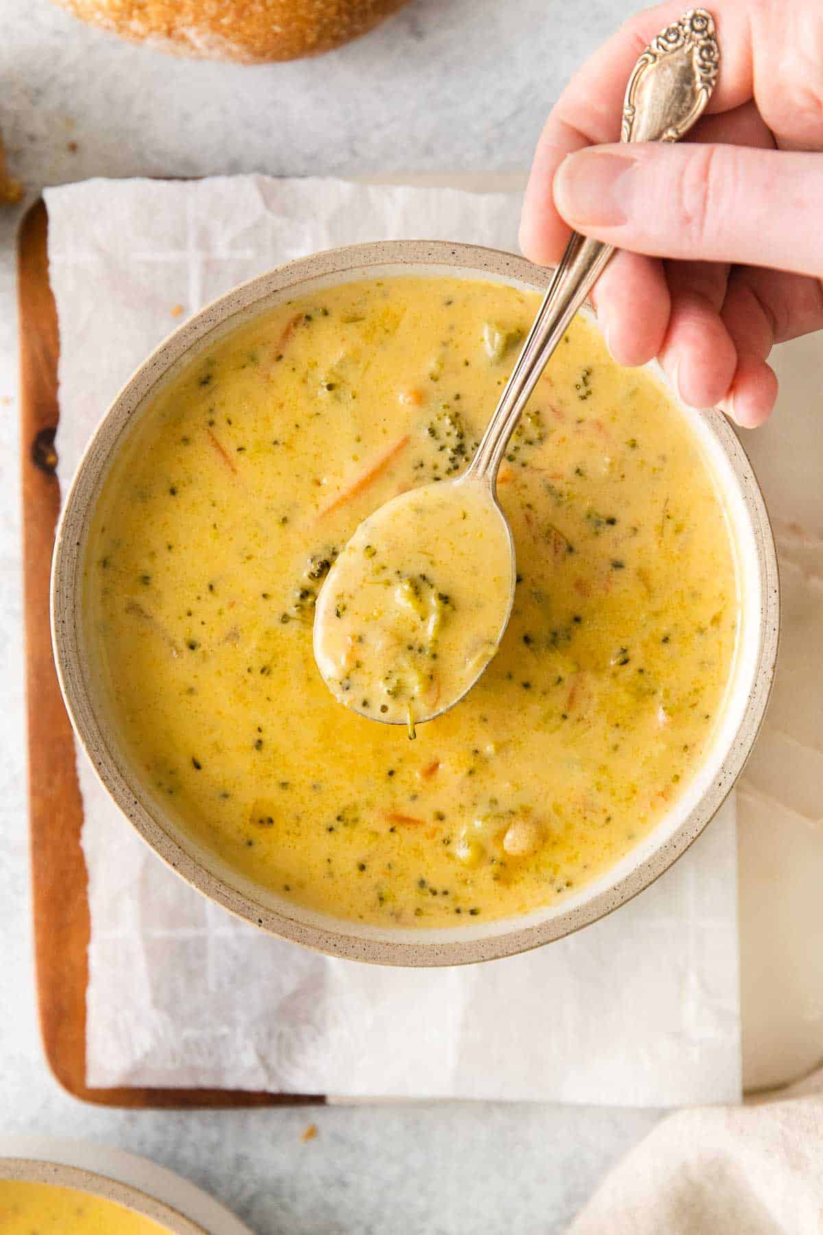 spoonful of broccoli cheese soup being held over a bowl full of soup.