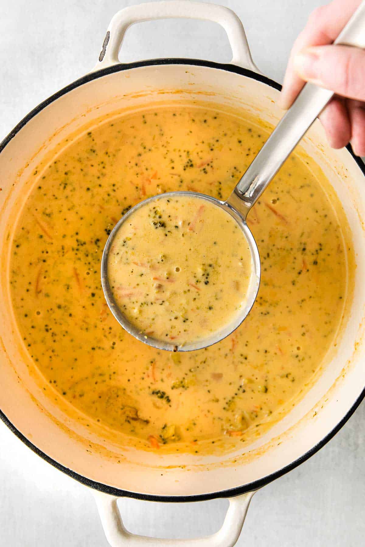 a ladle full of broccoli and cheese soup in a big white pot.
