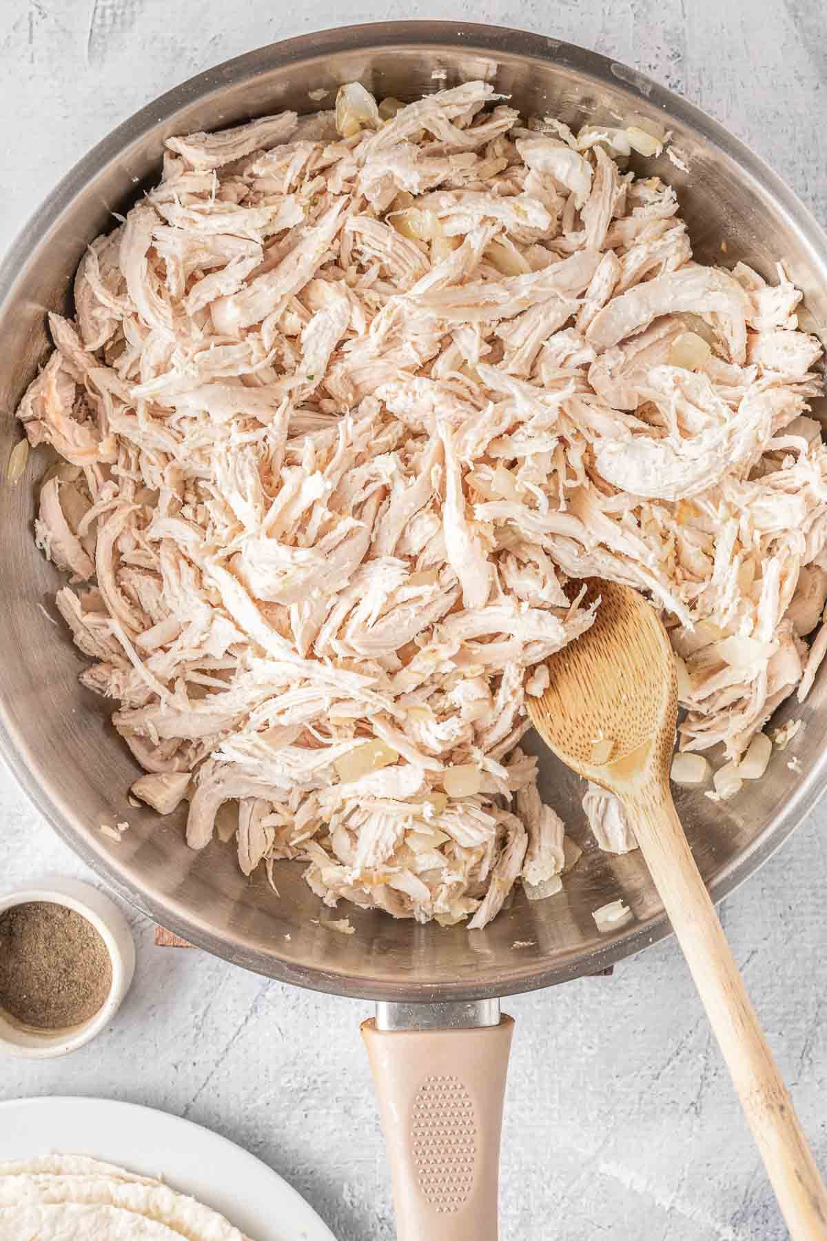 stainless steel skillet with cooked shredded chicken.