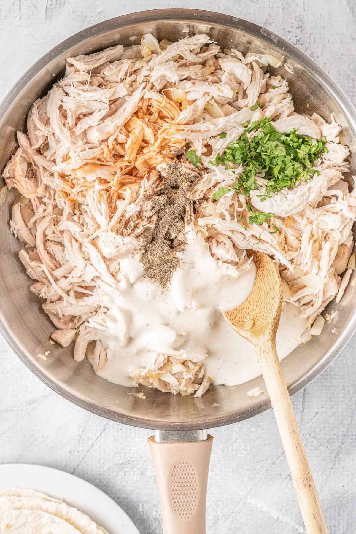 shredded cooked chicken topped with buffalo sauce, ranch dressing, and cilantro in a stainless steel skillet.