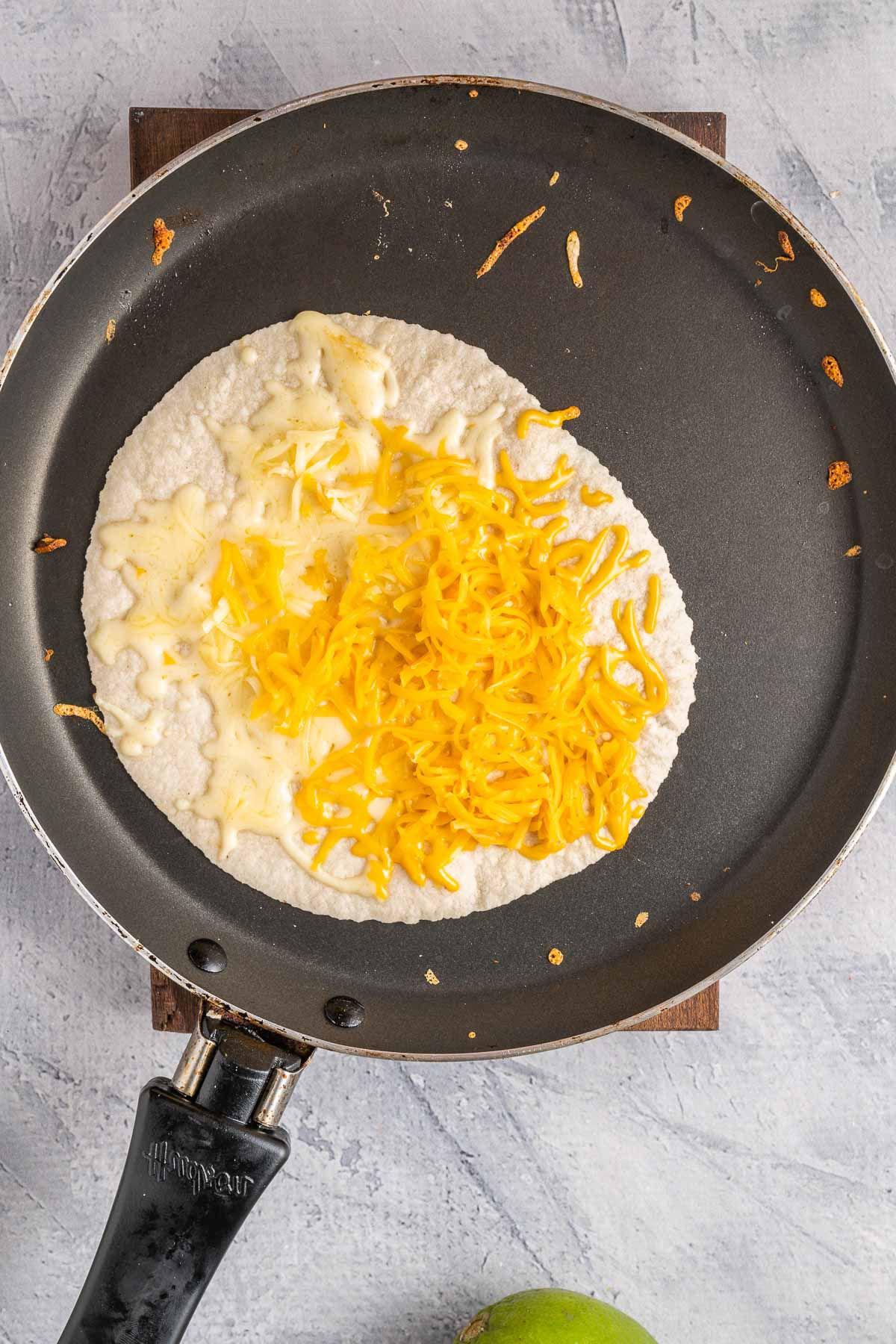 black skillet with a flour tortilla with shredded cheese.
