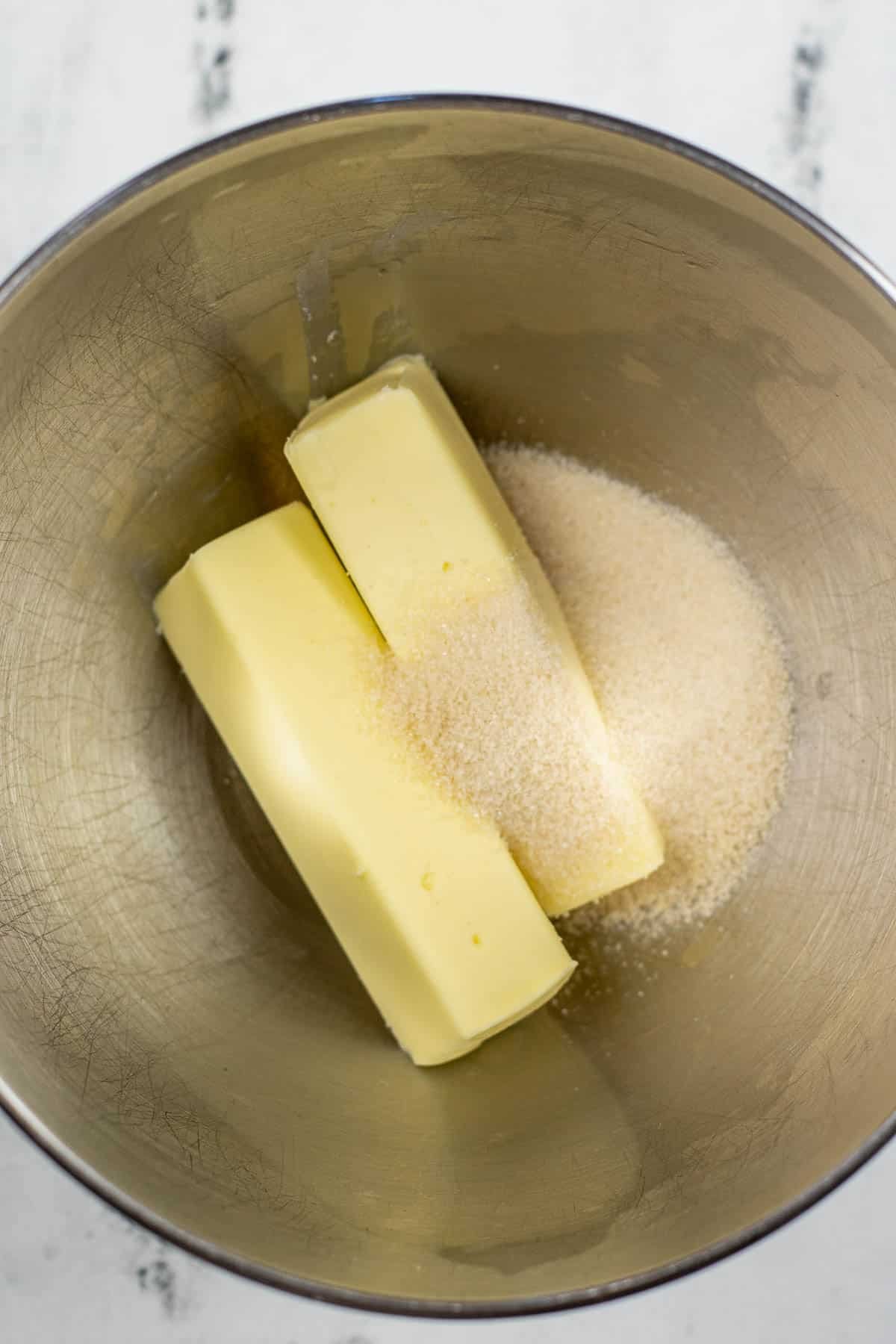 silver mixing bowl with two sticks of butter and sugar.