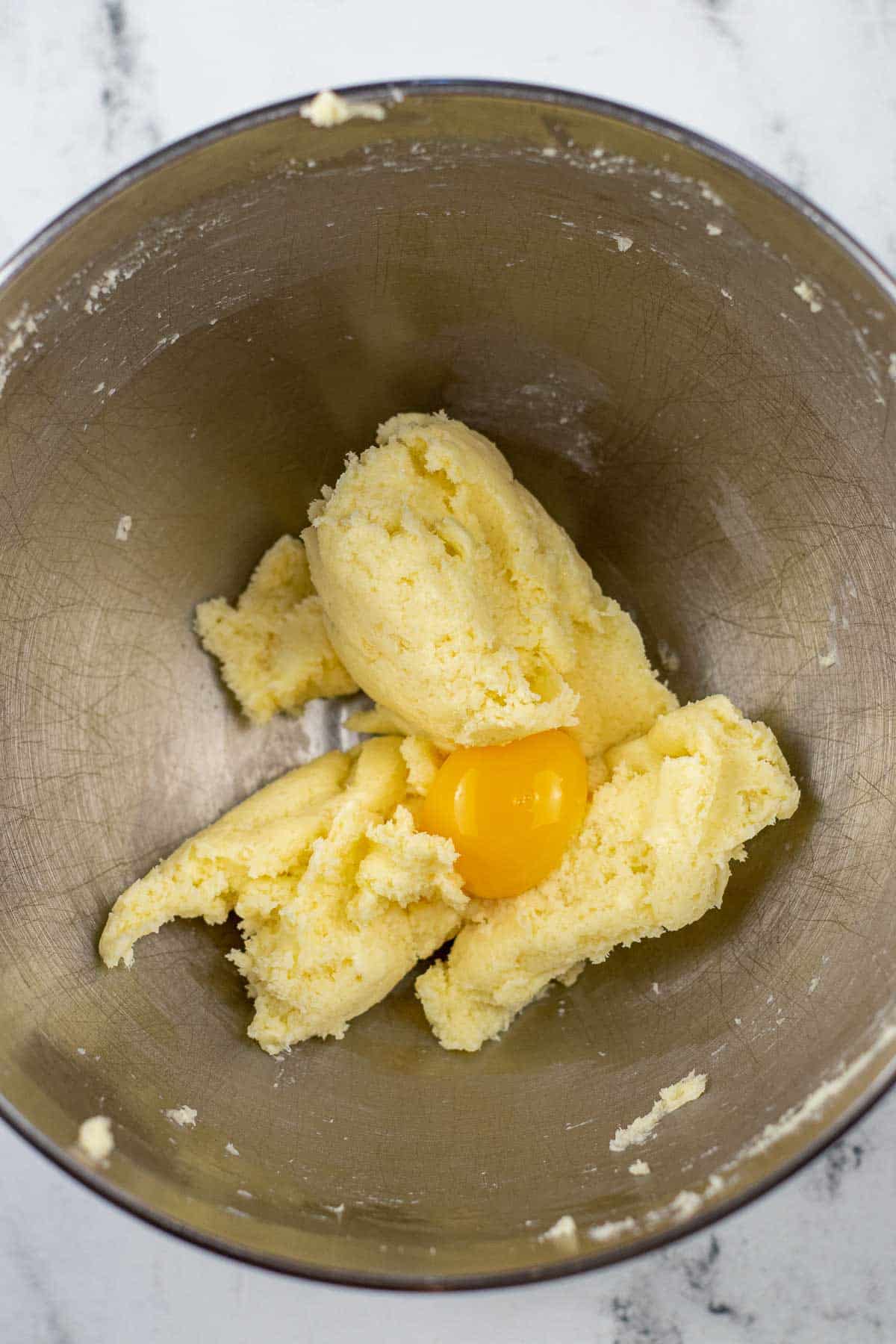 silver mixing bowl with sugar and butter creamed together and an egg yolk on top.