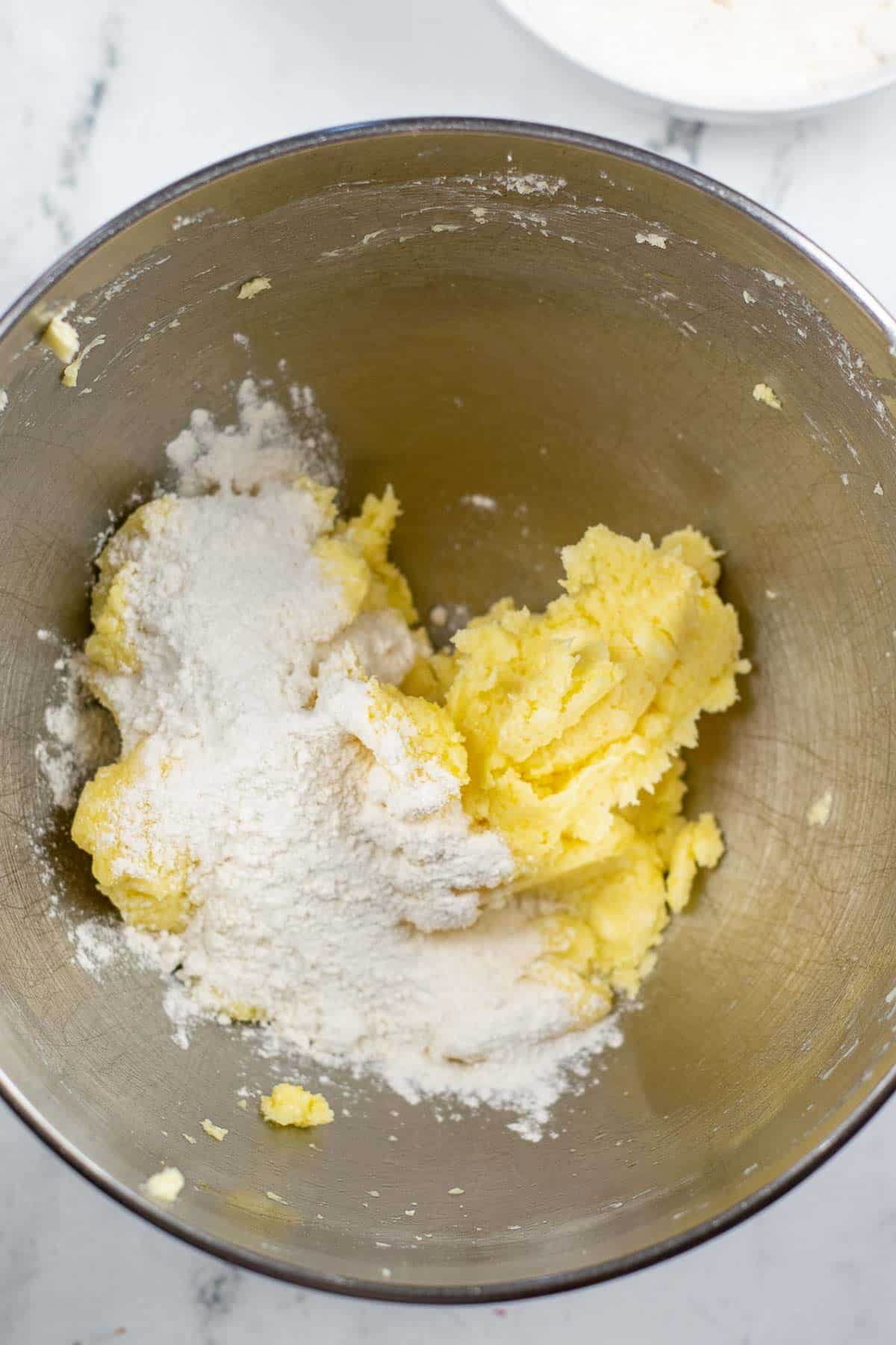 silver mixing bowl with egg and butter mixture with flour on top.