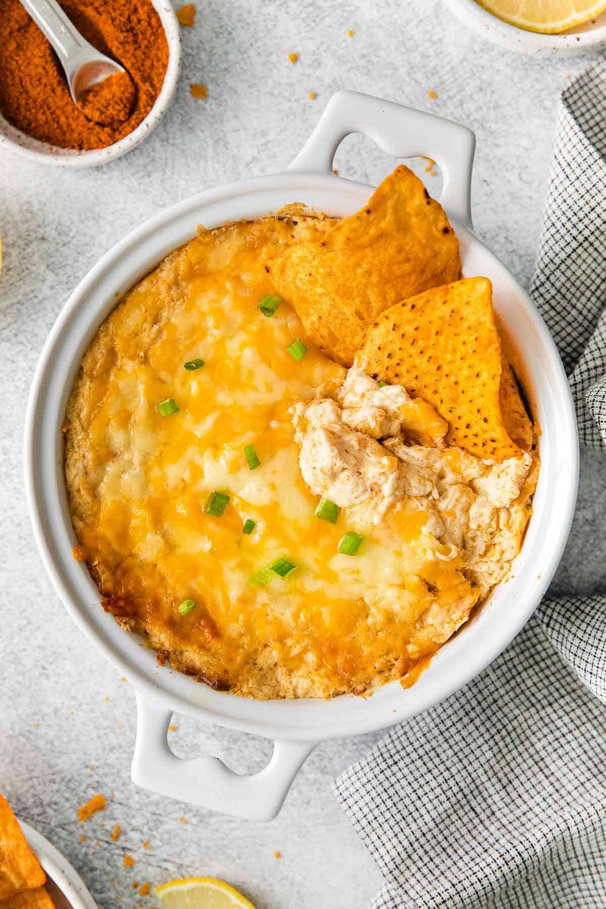 white baking dish full of hot cheesy crab dish with two tortilla chips dipped in.