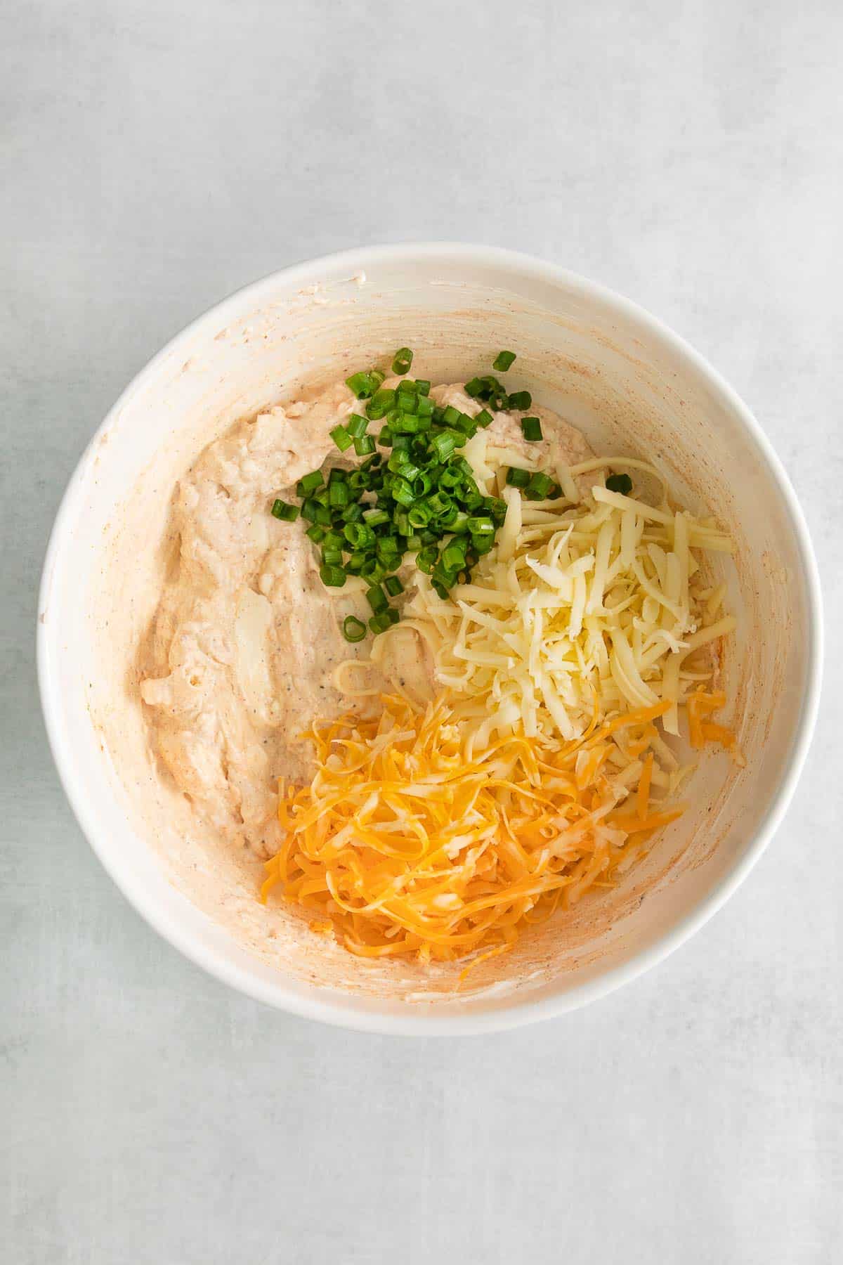 white bowl with shredded cheeses and sliced green onions.