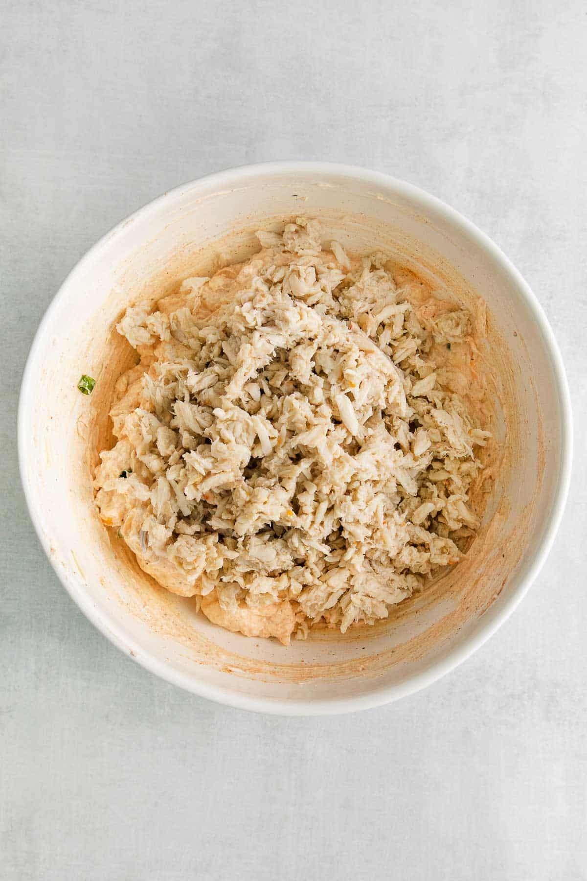 white bowl with raw lump crab meat over cream cheese and cheese mixture.
