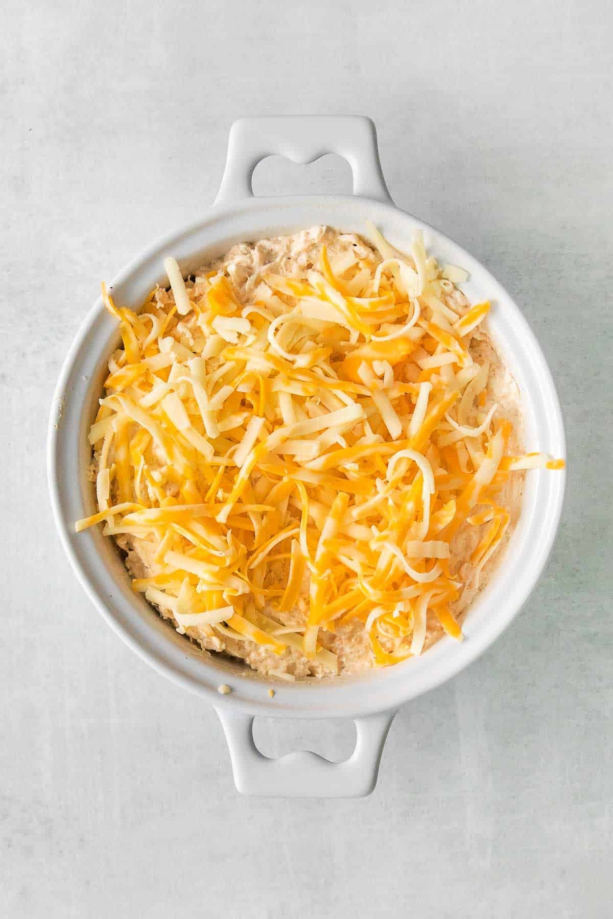white baking dish with crab dip topped with shredded cheese.
