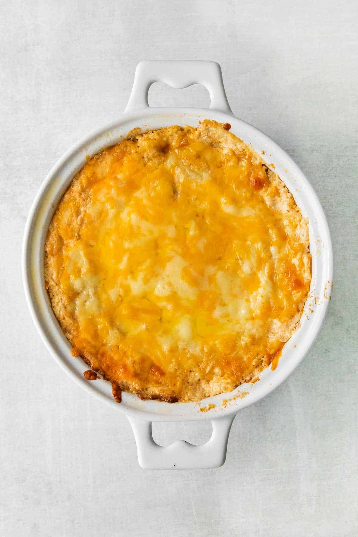 white round baking dish with melted cheese over crab dip.