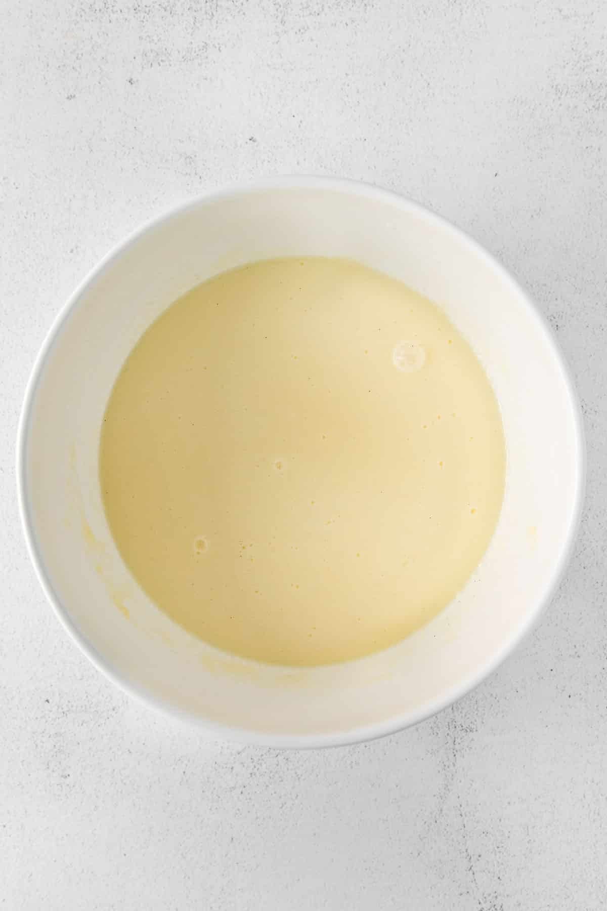white mixing bowl with milk, eggs, butter and sugar mixed together.