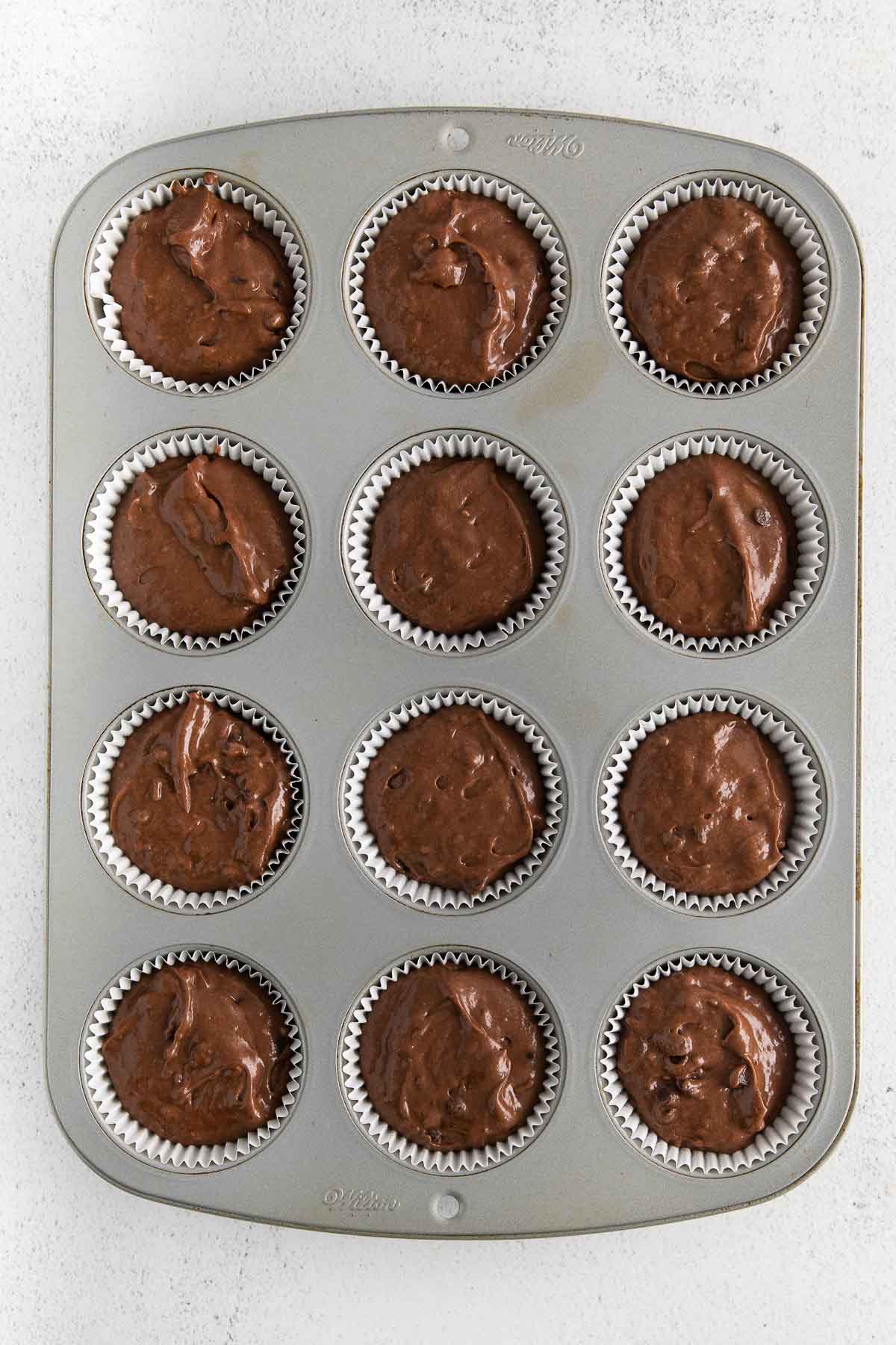 muffin tin with chocolate muffin batter in white paper liners.