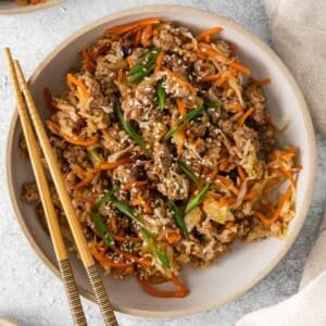 closeup of a bowl full a deconstructed egg roll in a bowl - browned ground pork, shredded cabbage and carrots topped with sesame seeds and sliced green onions.