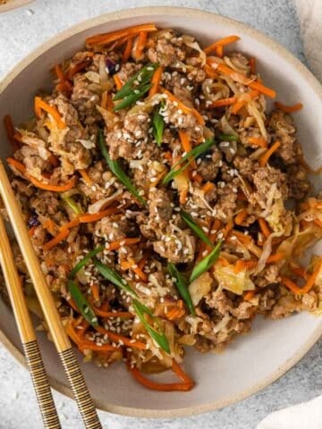 closeup of a bowl full a deconstructed egg roll in a bowl - browned ground pork, shredded cabbage and carrots topped with sesame seeds and sliced green onions.