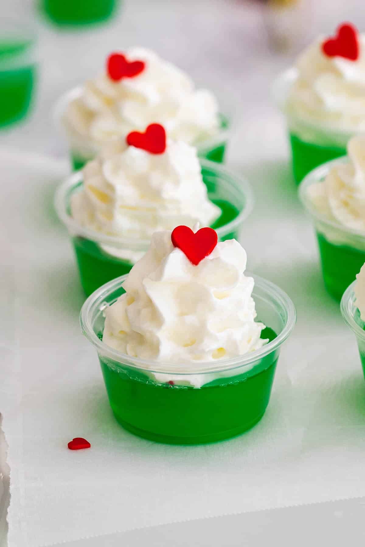 closeup of a grinch jello shot with whipped cream and a red candy heart on top.