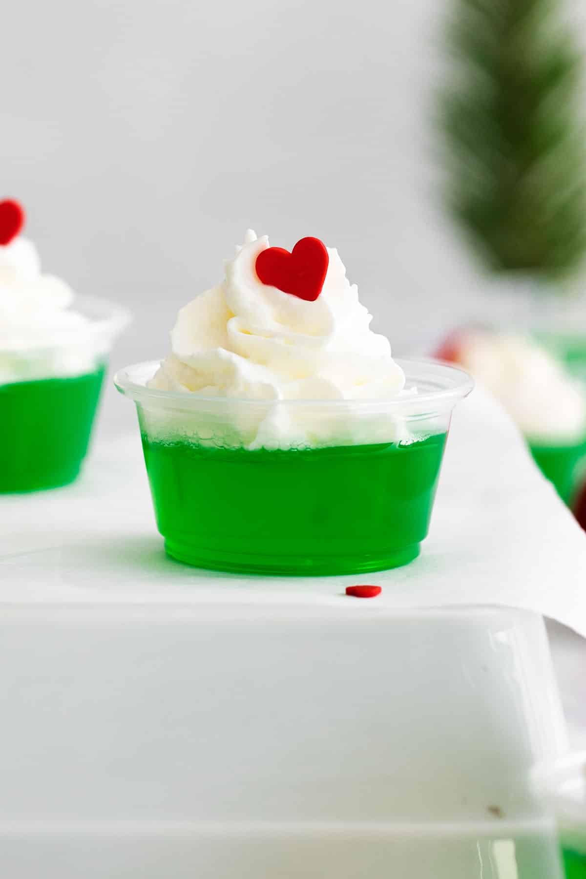 closeup of a grinch jello shot topped with whipped cream and a red heart.