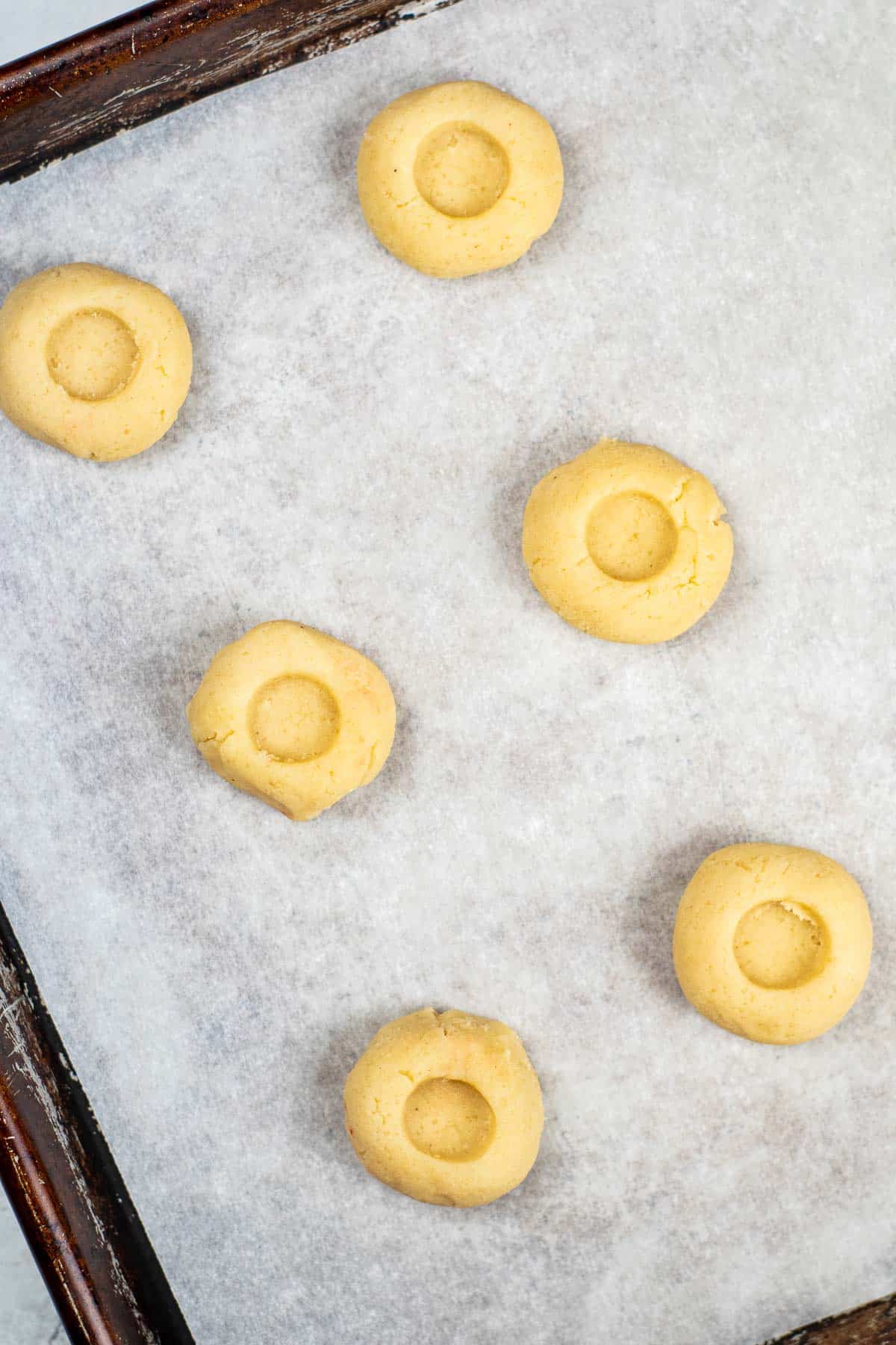 sugar cookie thumbprint cookie dough on parchment paper lined cookie sheet.