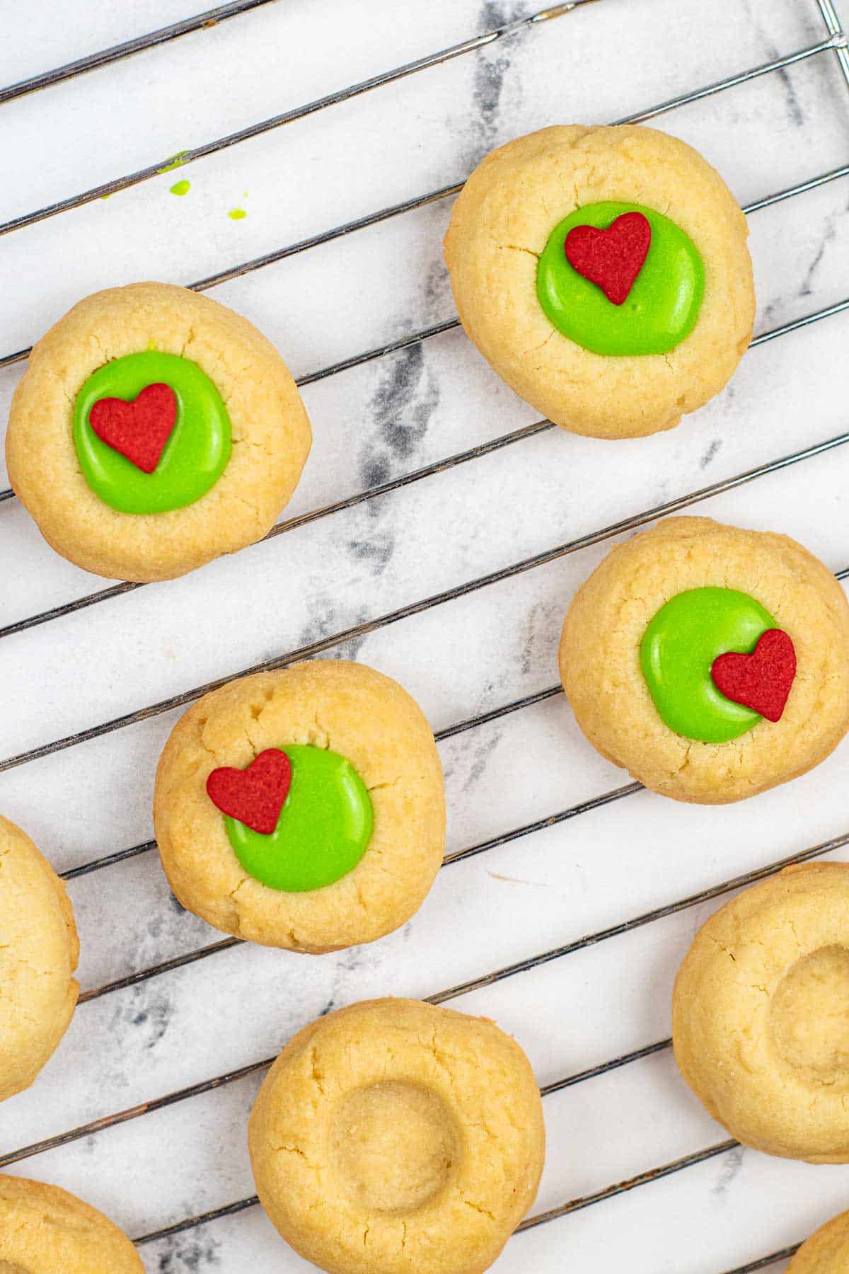 butter thumbprint cookies with green icing and a little red candy heart in the middle of some.